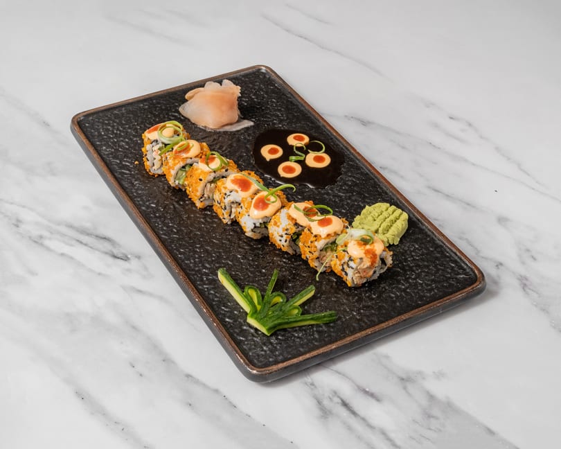 Sushi rolls with orange roe, sauce, green onions, pickled ginger, wasabi, and soy sauce.
