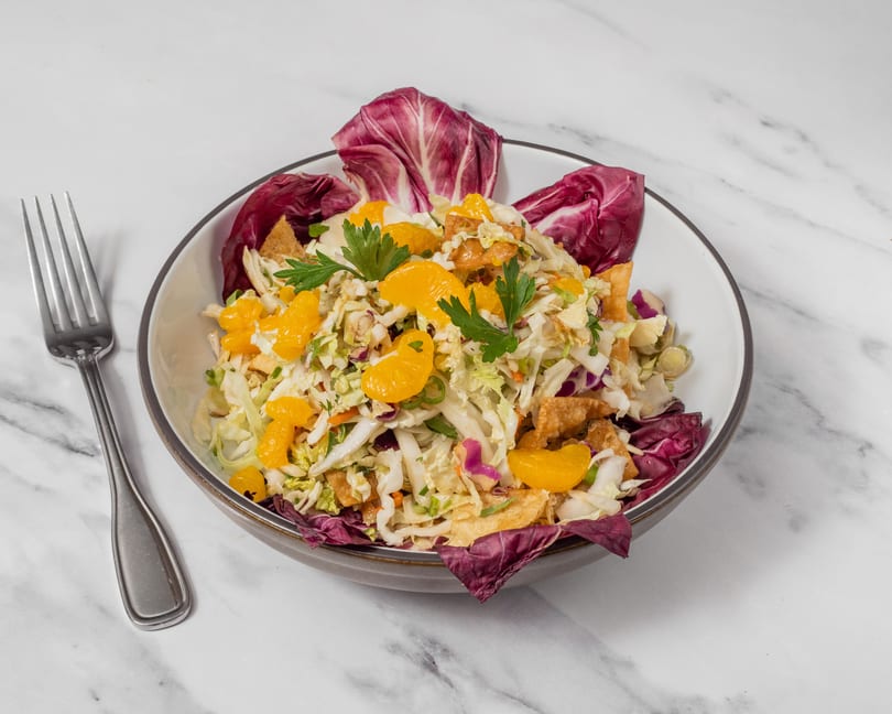 A vibrant salad with mandarin oranges, cabbage, wonton strips, and parsley in a bowl with a fork.